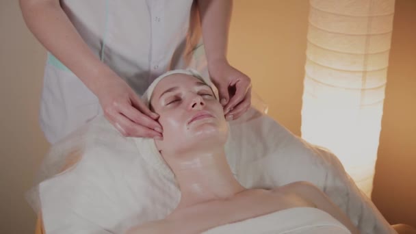 Professionele schoonheidsspecialiste maakt een complexe massage aan een jong meisje in het cosmetologie kantoor. — Stockvideo