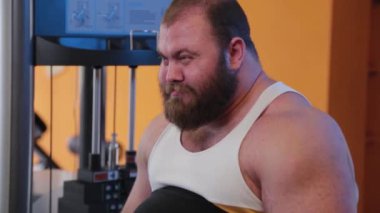 Çok büyük sakallı vücut geliştirici spor salonunda bacak çalıştırıyor..