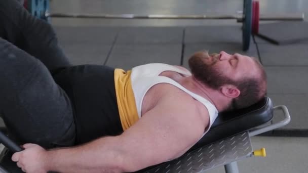 Stor och kraftfull tyngdlyftare tränar ben på simulatorn i gymmet. — Stockvideo
