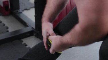 Büyük ve güçlü halterci dizlerine elastik sert bandajlar sarar..