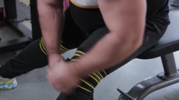 Grote en krachtige gewichtheffer wikkelt elastisch hard verband op zijn knieën. — Stockvideo