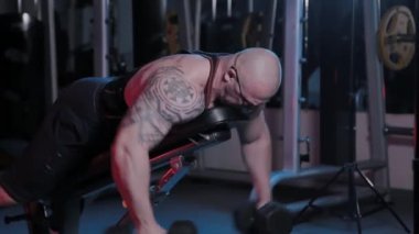 Profesyonel vücut geliştirici, spor kulübünde dambılları olan bir bankta deltoid kas çalıştırır..