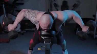 Profesyonel vücut geliştirici, spor kulübünde dambılları olan bir bankta deltoid kas çalıştırır..