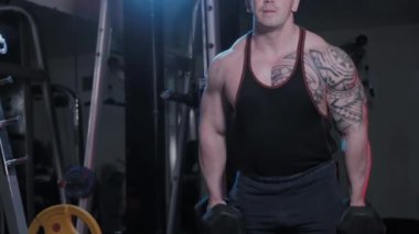 Profesyonel vücut geliştirici, bir spor kulübünde dambıllı bisepsler eğitir..