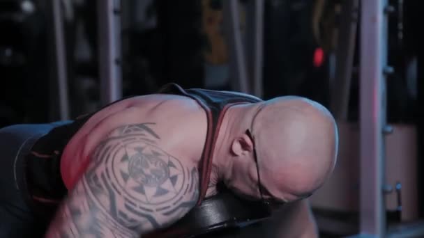 Professional bodybuilder trains back deltoid muscle on a bench with dumbbells in a sports club. — Stock Footage Professional bodybuilder trains back deltoid muscle on a bench with dumbbells in a sports club. Stock Footage