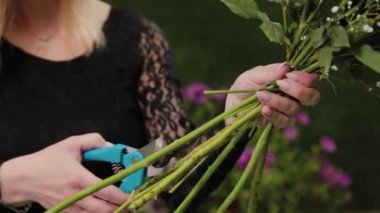 Çiçekçi makasla buket yapmak için çiçek saplarını kesiyor..