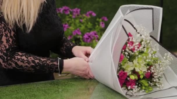 Florista embala um buquê de flores em um belo papel . — Vídeo de Stock