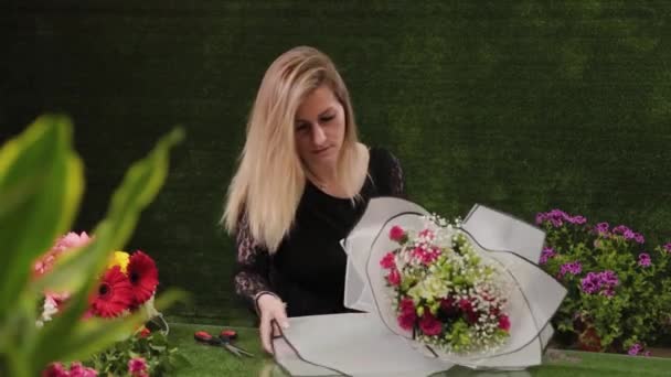 Florista embala um buquê de flores em um belo papel . — Vídeo de Stock