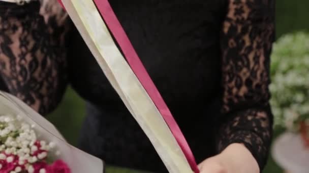Florista mulher profissional desenrola a fita vermelha, corta com tesoura para embalar o buquê . — Vídeo de Stock