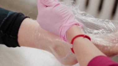 Pedikür ustası bir kızın bacaklarını folyoyla sarıyor..