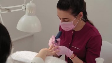 Manikürcü, manikür salonundaki bir müşteriye makineyle tırnak kesiyor..