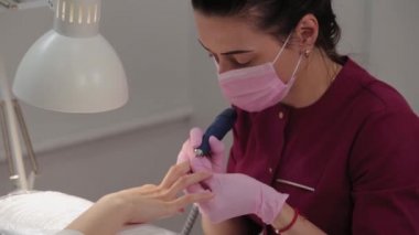 Manikürcü, manikür salonundaki bir müşteriye makineyle tırnak kesiyor..