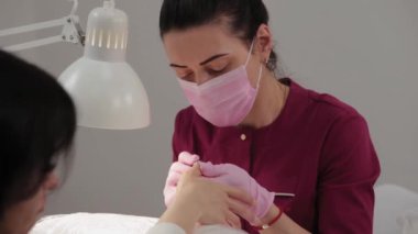 Manikürcü, manikür salonundaki bir müşteriye makineyle tırnak kesiyor..