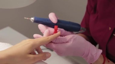 Manikürcü, manikür salonundaki bir müşteriye makineyle tırnak kesiyor..