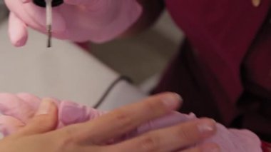 Manikürcü bir müşteriyle güzellik salonunda tırnaklarını cilalıyor..