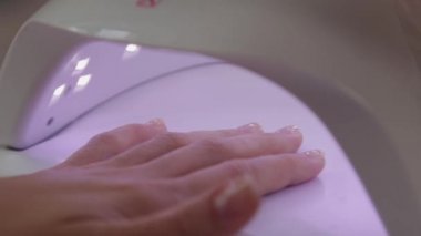 Kadın evde tek başına kırmızı jel cilasıyla oje sürüyor. Manikür için ultraviyole lamba. Ellerle çalışmanın modern metodu. Ultraviyole alet, ana ekipman.