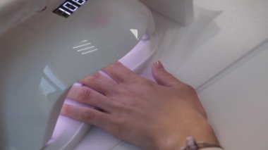 Kadın evde tek başına kırmızı jel cilasıyla oje sürüyor. Manikür için ultraviyole lamba. Ellerle çalışmanın modern metodu. Ultraviyole alet, ana ekipman.