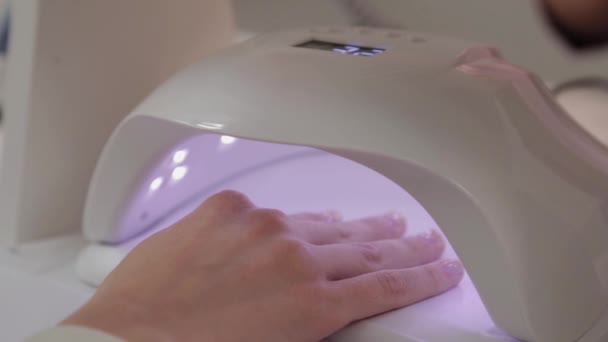 Vrouw verf nagels met rode gel polijsten alleen thuis. Uv led lamp voor het drogen van manicure. Moderne methode van werken met handen. Ultraviolet instrument, basisuitrusting. — Stockvideo