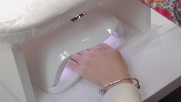 Vrouw verf nagels met rode gel polijsten alleen thuis. Uv led lamp voor het drogen van manicure. Moderne methode van werken met handen. Ultraviolet instrument, basisuitrusting. — Stockvideo