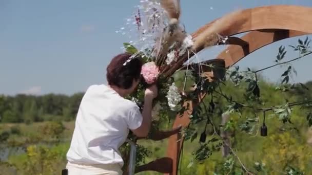 Decorador de bodas decora el lugar de registro del matrimonio con flores frescas . — Vídeo de stock