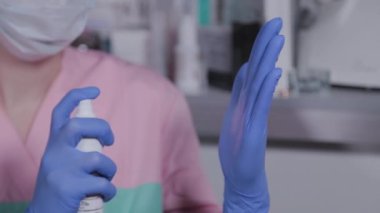 Profesyonel güzellik uzmanı mavi lastik eldivenleri antiseptikle tedavi ediyor.