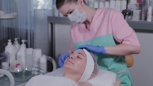 Profesionální kosmetička nasazuje klobouk na klienta na ženu. — Stock video