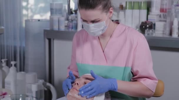 Professionele schoonheidsspecialiste wast een vrouw en masseert haar gezicht. — Stockvideo