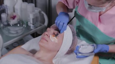 Profesyonel güzellik uzmanı bir kadına yüz maskesi takıyor..