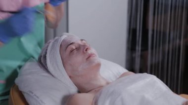 Profesyonel güzellik uzmanı bir kadına yüz maskesi takıyor..