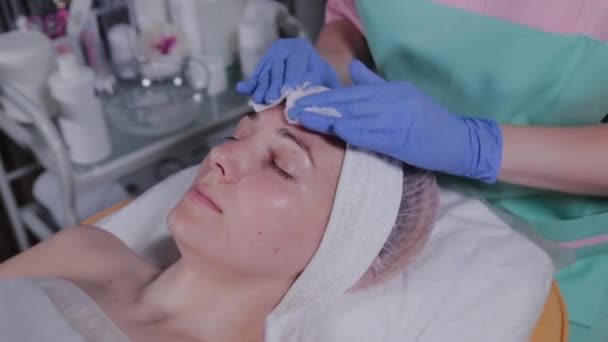 Esteticista profissional limpa um rosto de mulher com almofadas de algodão . — Vídeo de Stock