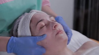 Güzellik uzmanı güzellik salonunda bir kadına yüz masajı yapıyor..