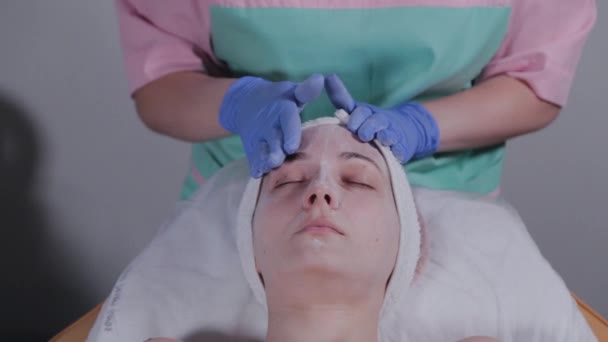 Esteticista faz massagem facial a uma mulher em um salão de beleza . — Vídeo de Stock