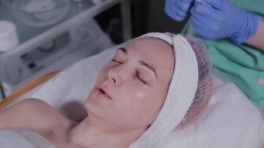 Profesyonel güzellik uzmanı bir kadının yüzünü pamukla siliyor..