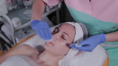Profesyonel güzellik uzmanı bir kadının yüzünü pamukla siliyor..
