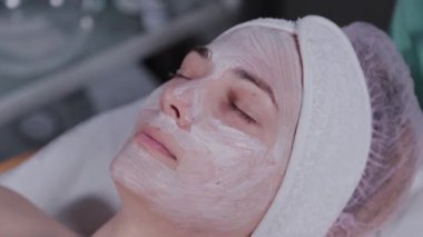 Profesyonel güzellik uzmanı bir kadına yüz maskesi takıyor..