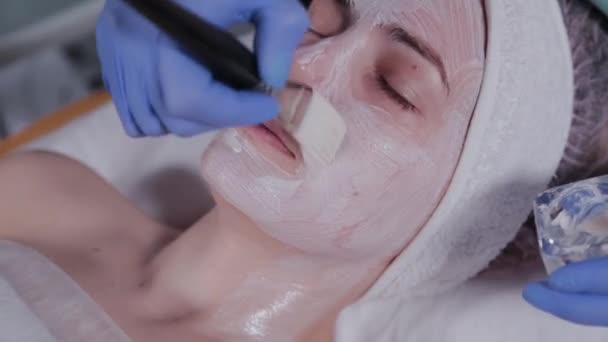 Επαγγελματίας αισθητικός που εφαρμόζει μάσκα προσώπου σε μια γυναίκα. — Αρχείο Βίντεο