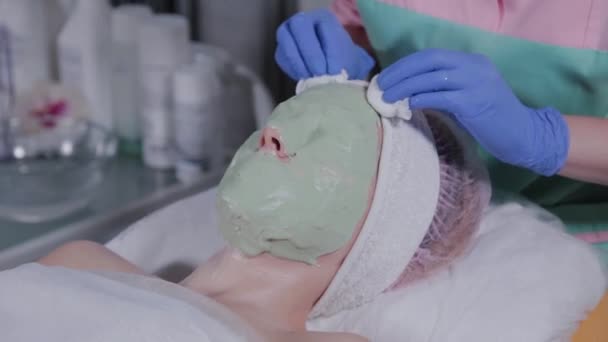 Professionell kosmetolog tar bort masken från ansiktet på en kvinna. — Stockvideo