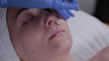 Profesyonel güzellik uzmanı güzellik salonundaki bir kadının yüzüne krem sürüyor..