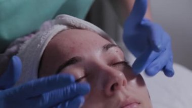 Profesyonel güzellik uzmanı güzellik salonundaki bir kadının yüzüne krem sürüyor..