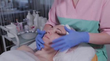 Profesyonel güzellik uzmanı güzellik salonunda bir kadına yüz masajı yapar..