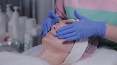 Profesyonel güzellik uzmanı güzellik salonunda bir kadına yüz masajı yapar..