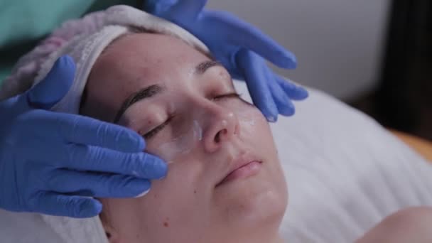 Esteticista profesional aplica crema en la cara de una mujer en un salón de belleza . — Vídeo de stock