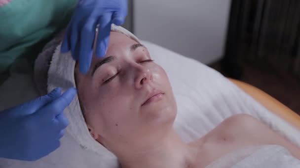 Ahli kecantikan profesional menerapkan krim di wajah seorang wanita di sebuah salon kecantikan. — Stok Video