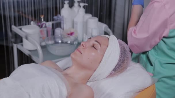 Professionelle Kosmetikerin cremt das Gesicht einer Frau in einem Schönheitssalon ein. — Stockvideo