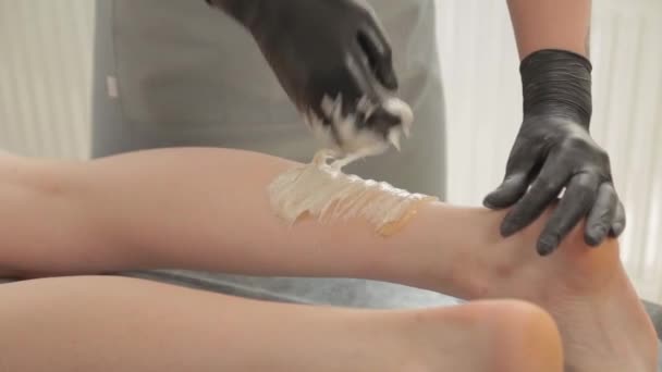 Beautist gör shugaring på benen på en ung kvinna. — Stockvideo