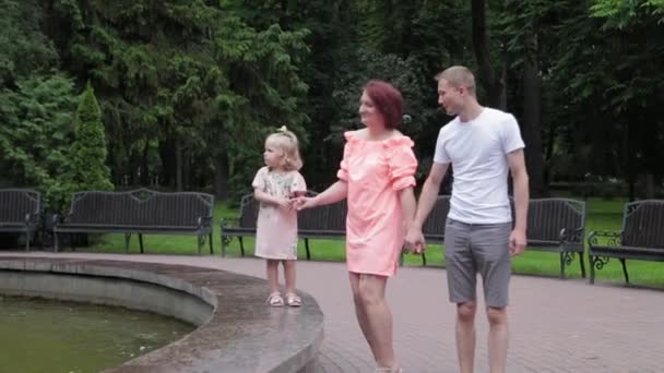 Eine junge Familie mit Kind spaziert am Brunnen. — Stockvideo