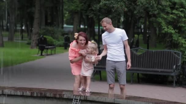 Eine junge Familie mit Kind spaziert am Brunnen. — Stockvideo