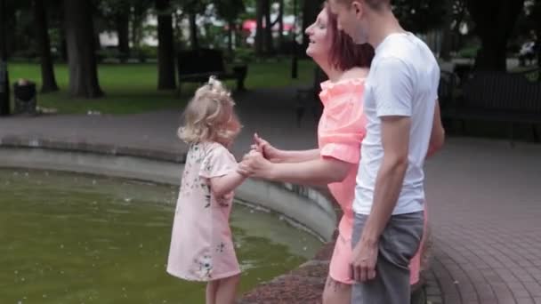 En ung familj med ett barn går vid fontänen. — Stockvideo
