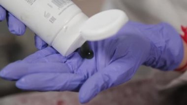Profesyonel güzellik uzmanı eldivenlere jöle sürer ve ovalar..