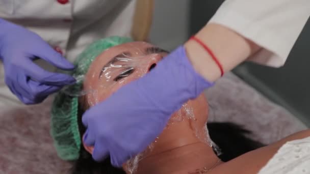 Um esteticista profissional aplica um filme no rosto . — Vídeo de Stock